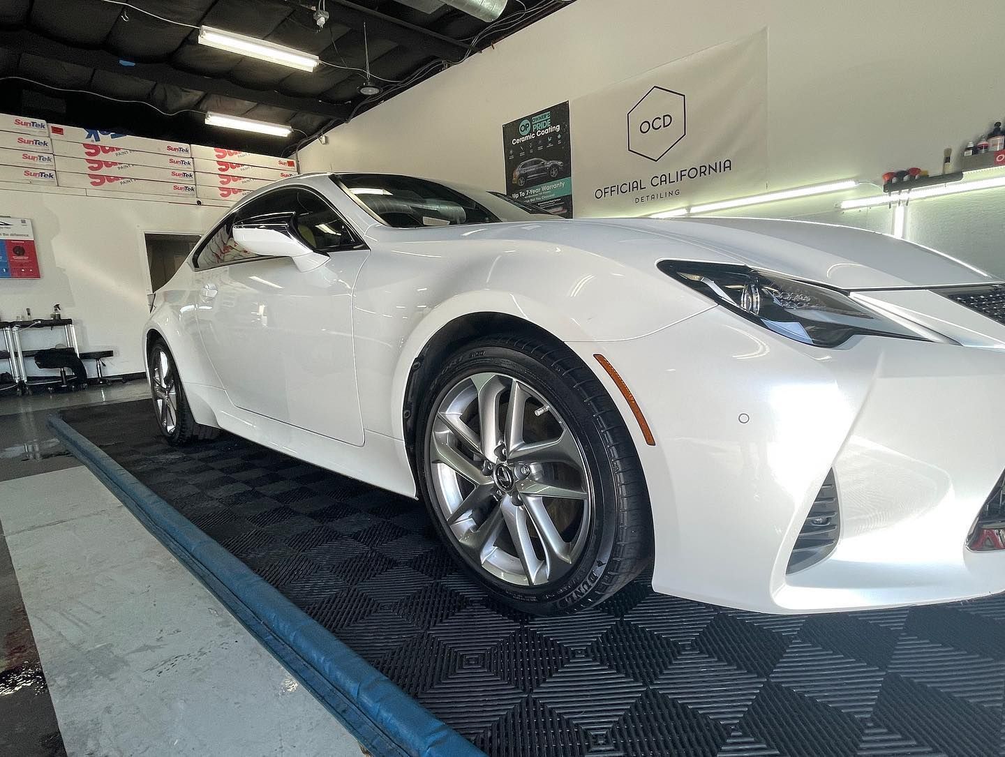 A white sports car is parked on a ramp in a garage.