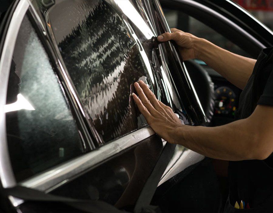 A person is applying tinted window film to a car window.