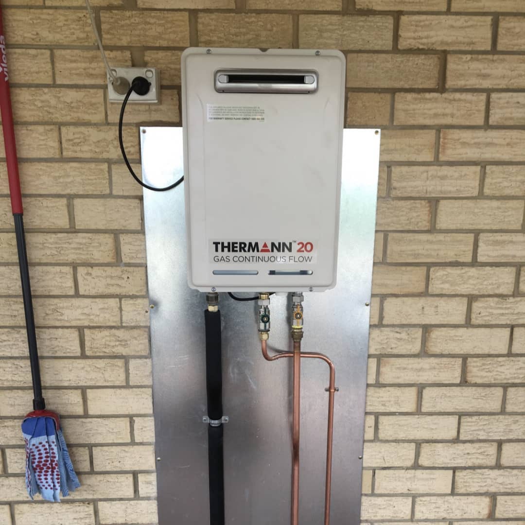 A white water heater is mounted to a brick wall