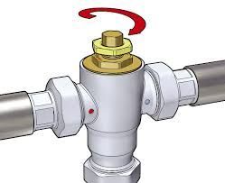 a close up of a tempering valve on a pipe with a red arrow pointing to it pointing which way to turn the tempering valve to adjust the temperture