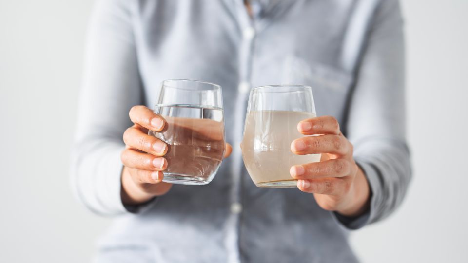 Person holding two glasses of water, one clear, one murky.