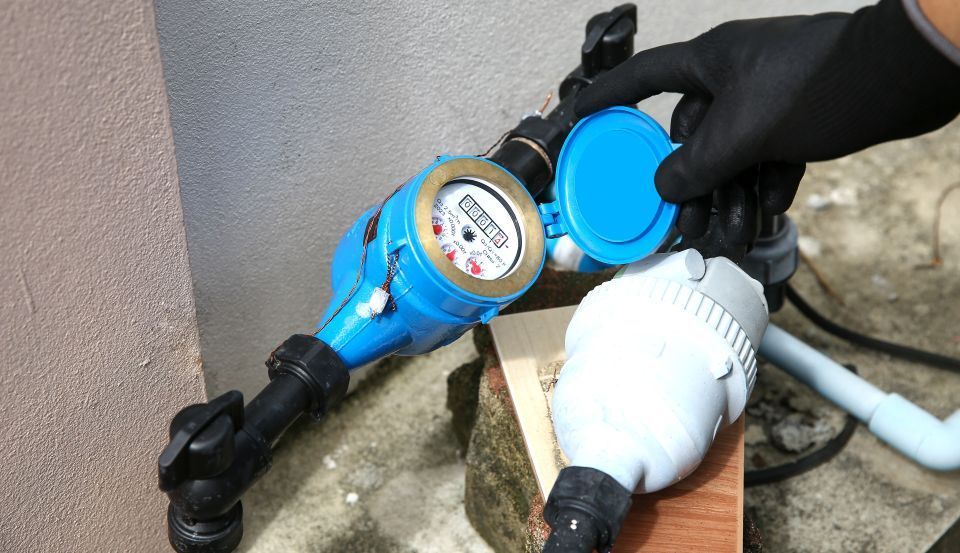 Hand in black glove opens a blue house water meter cover.