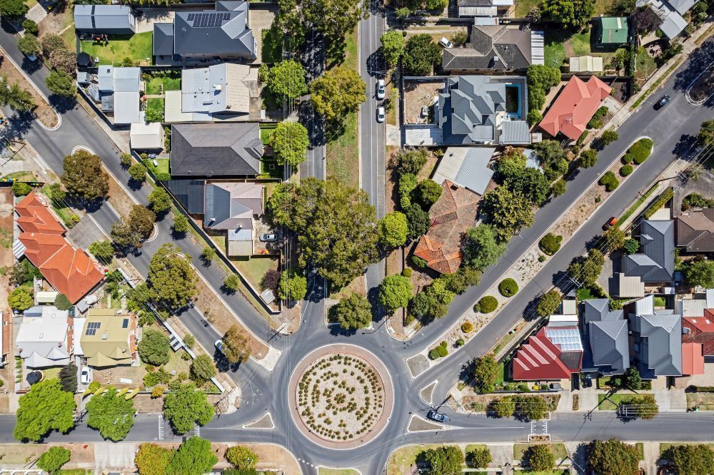 Aerial view of a suburban neighborhood with houses, streets, and a roundabout at the center intersection.