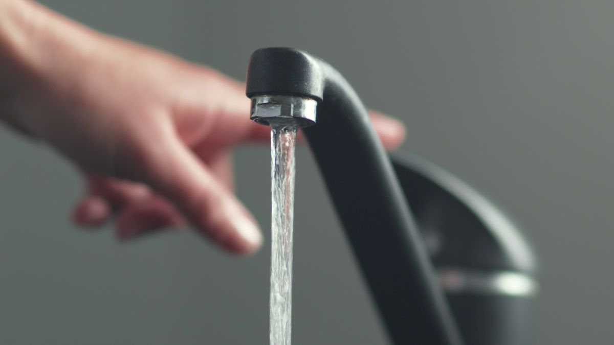 A hand turning off a black faucet likely causing water hammering