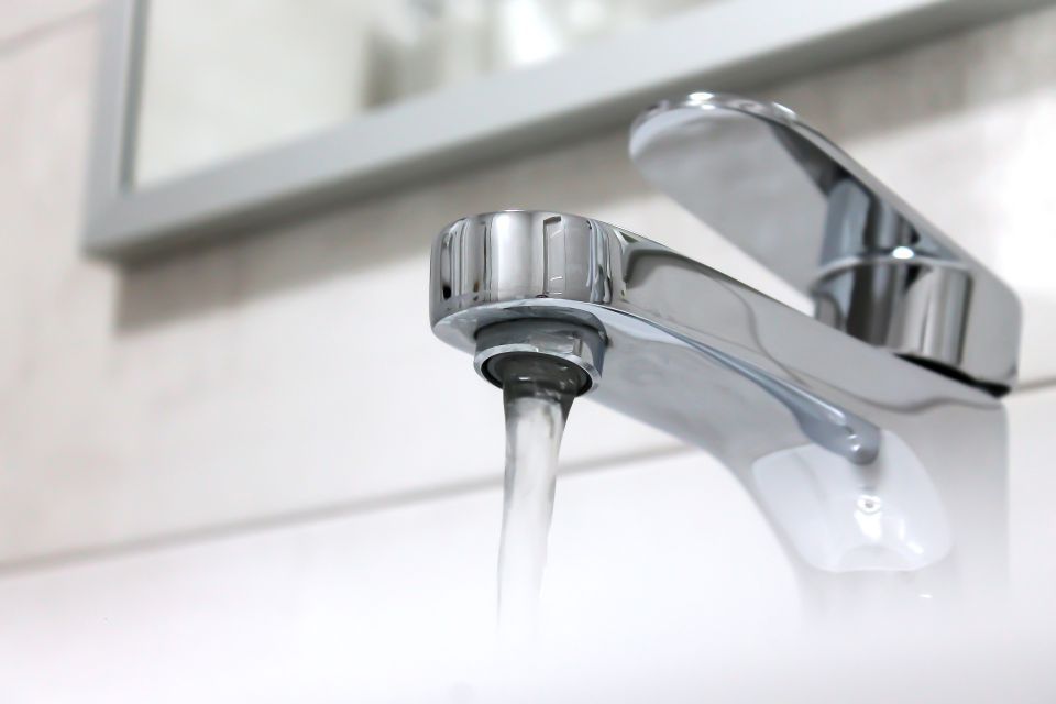 Average water usage: A chrome bathroom faucet flowing with water, positioned above a white sink with a mirror visible in the background.