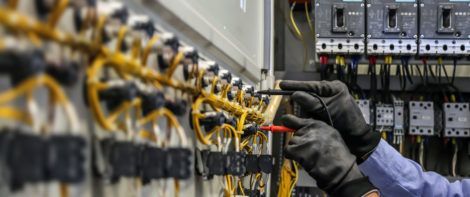 Electrician testing wires in an electrical panel, wearing black gloves.