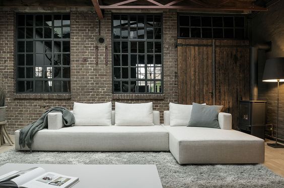 Een woonkamer met een grote witte bank van Sur&Plus en een bakstenen muur.