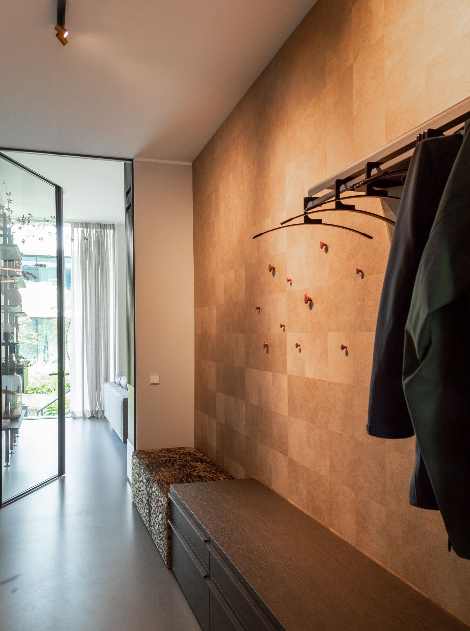 Een entree met een behang van Elitis en kleding aan de muur