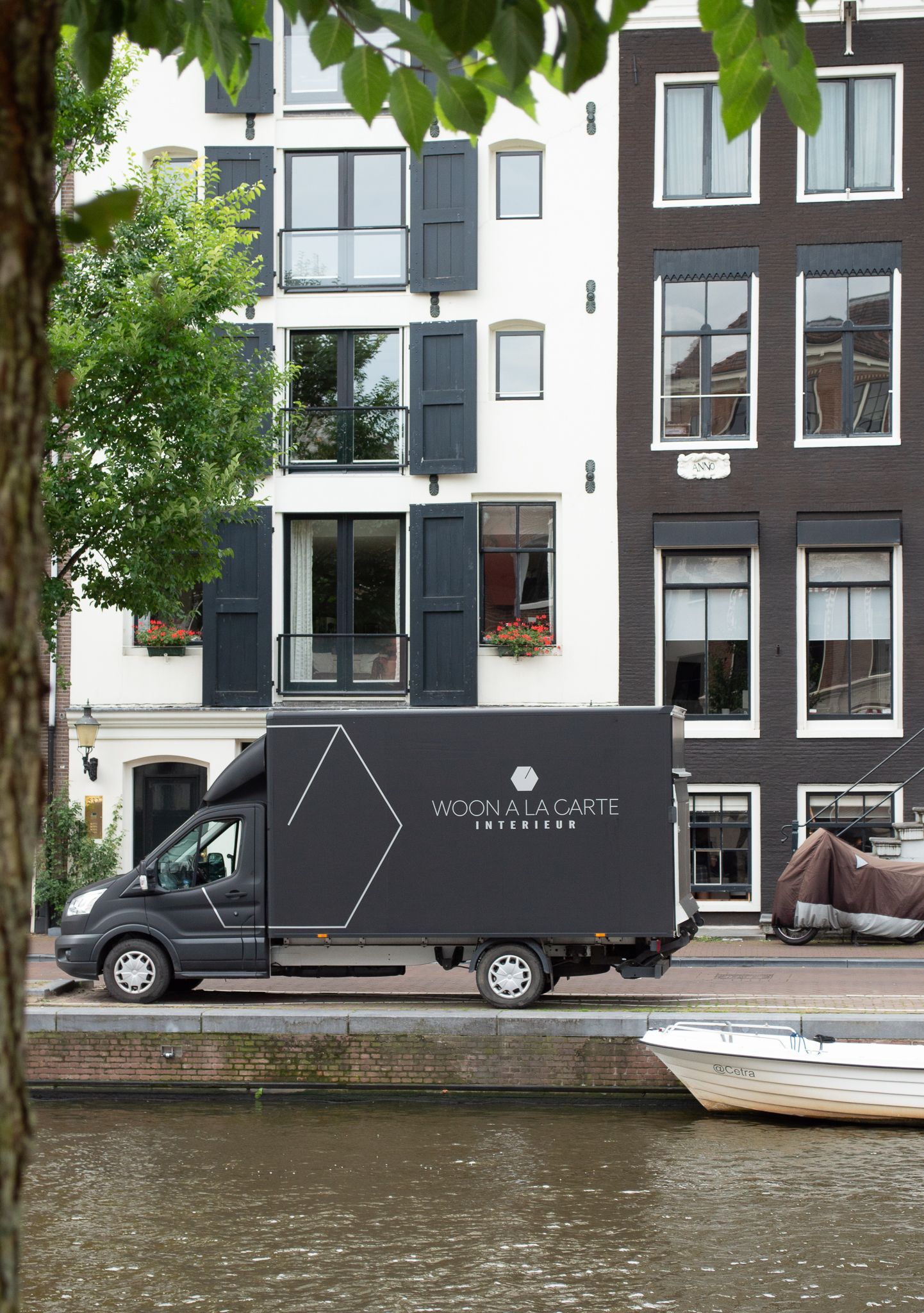 Een zwarte bestelwagen van Woon à la carte staat geparkeerd op de Prinsengracht in Amsterdam
