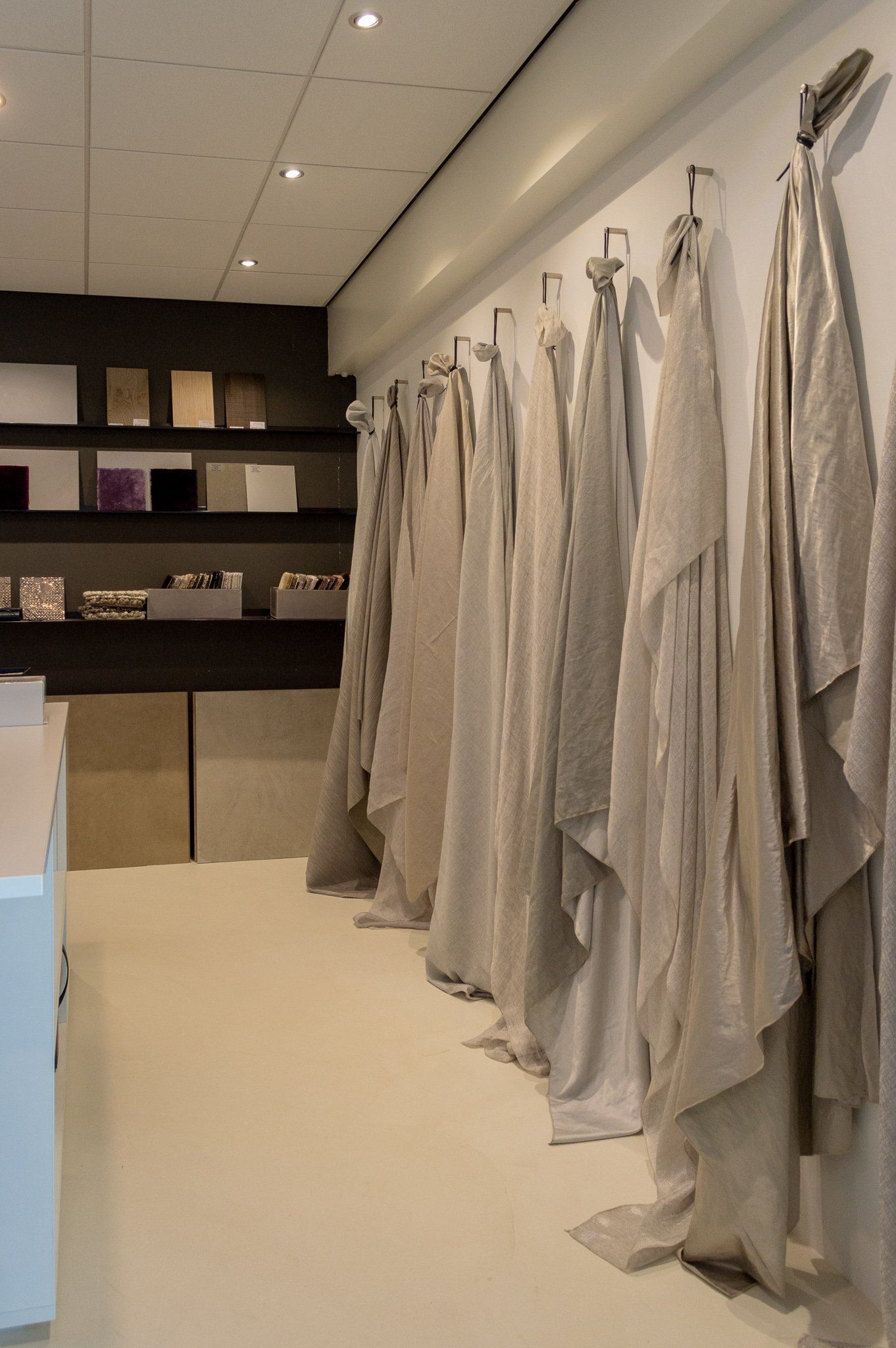 Een rij gordijnstoffen die aan een muur in een winkel hangen. Linnen, hennep, wol, katoen.