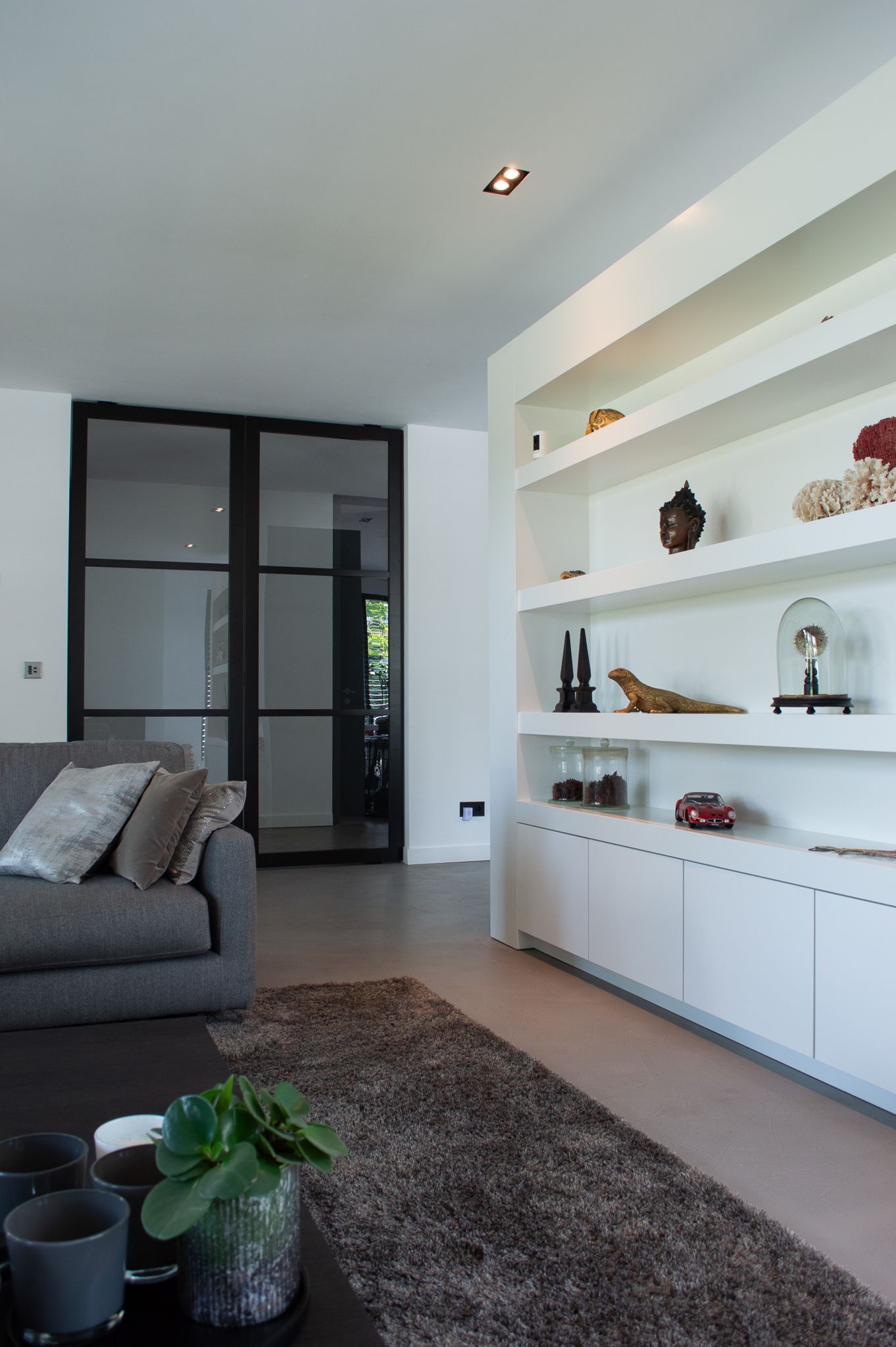 Een woonkamer met een grijze bank en witte planken