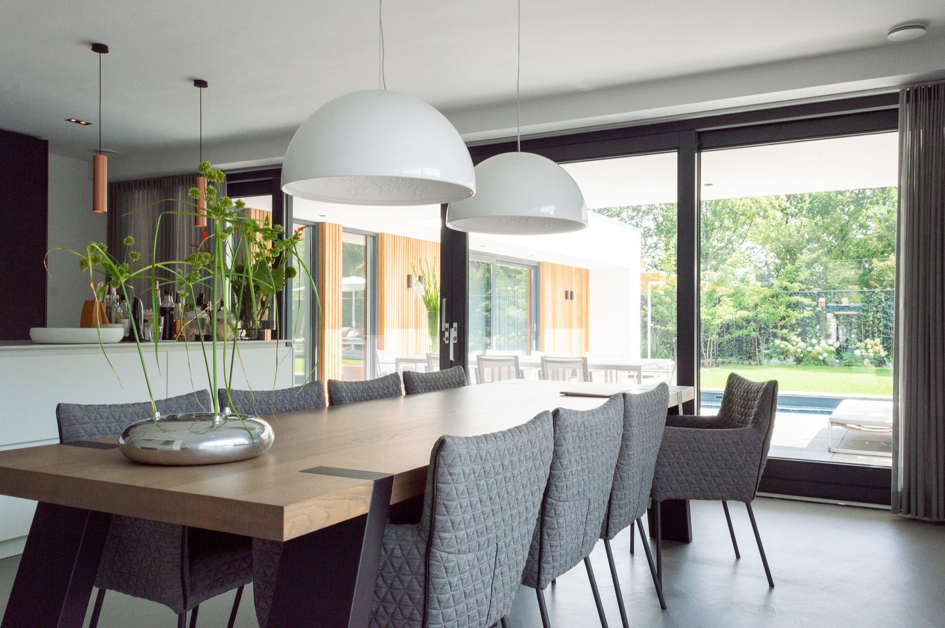 Een eetkamer met een lange tafel van Van Seuren tafels, stoelen van Label en een glazen schuifdeur.