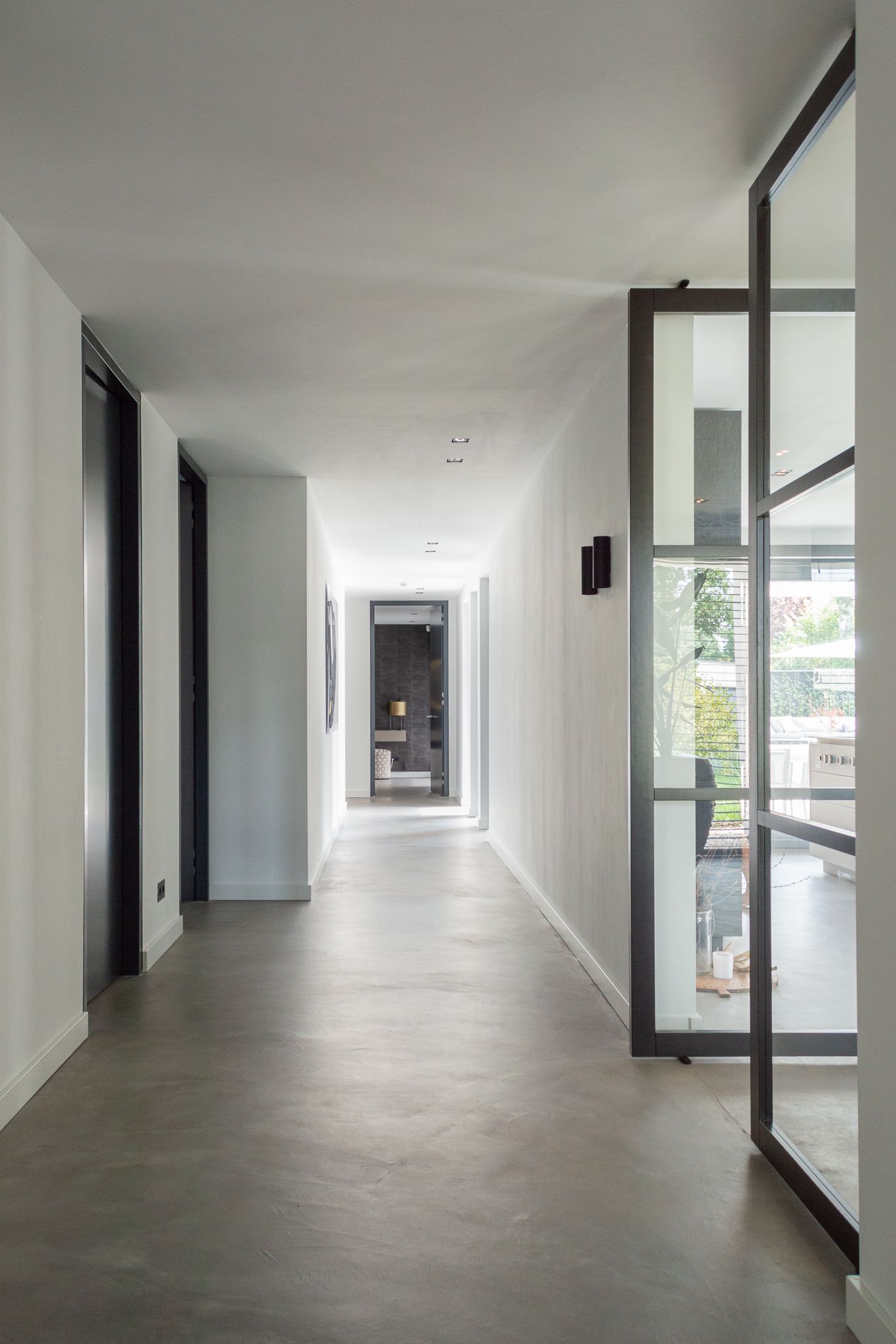 Een lange gang met een glazen deur die naar de woonkamer leidt.