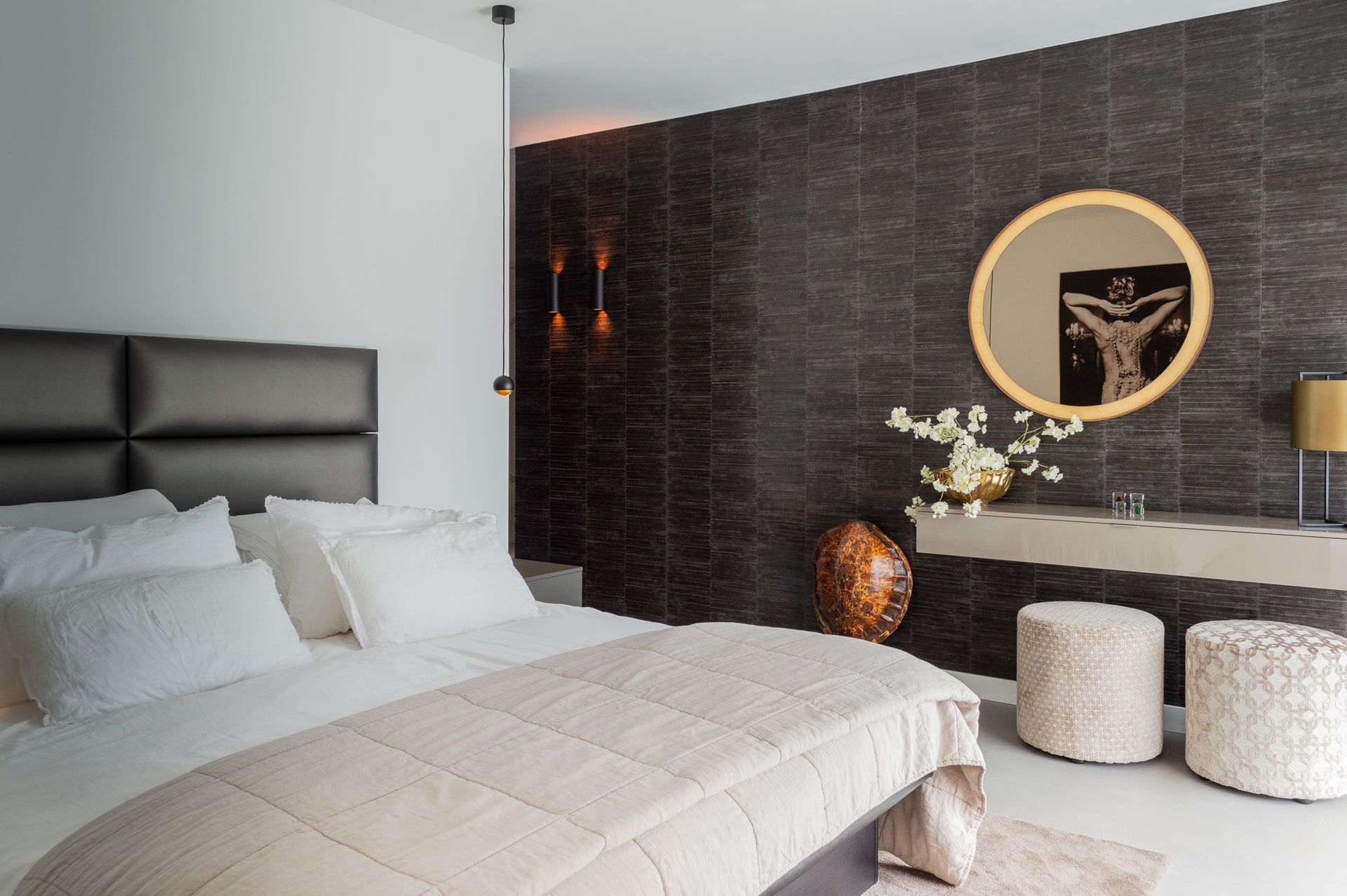 Een slaapkamer met een groot bed van Nilson Bedsen een ronde spiegel aan de muur.