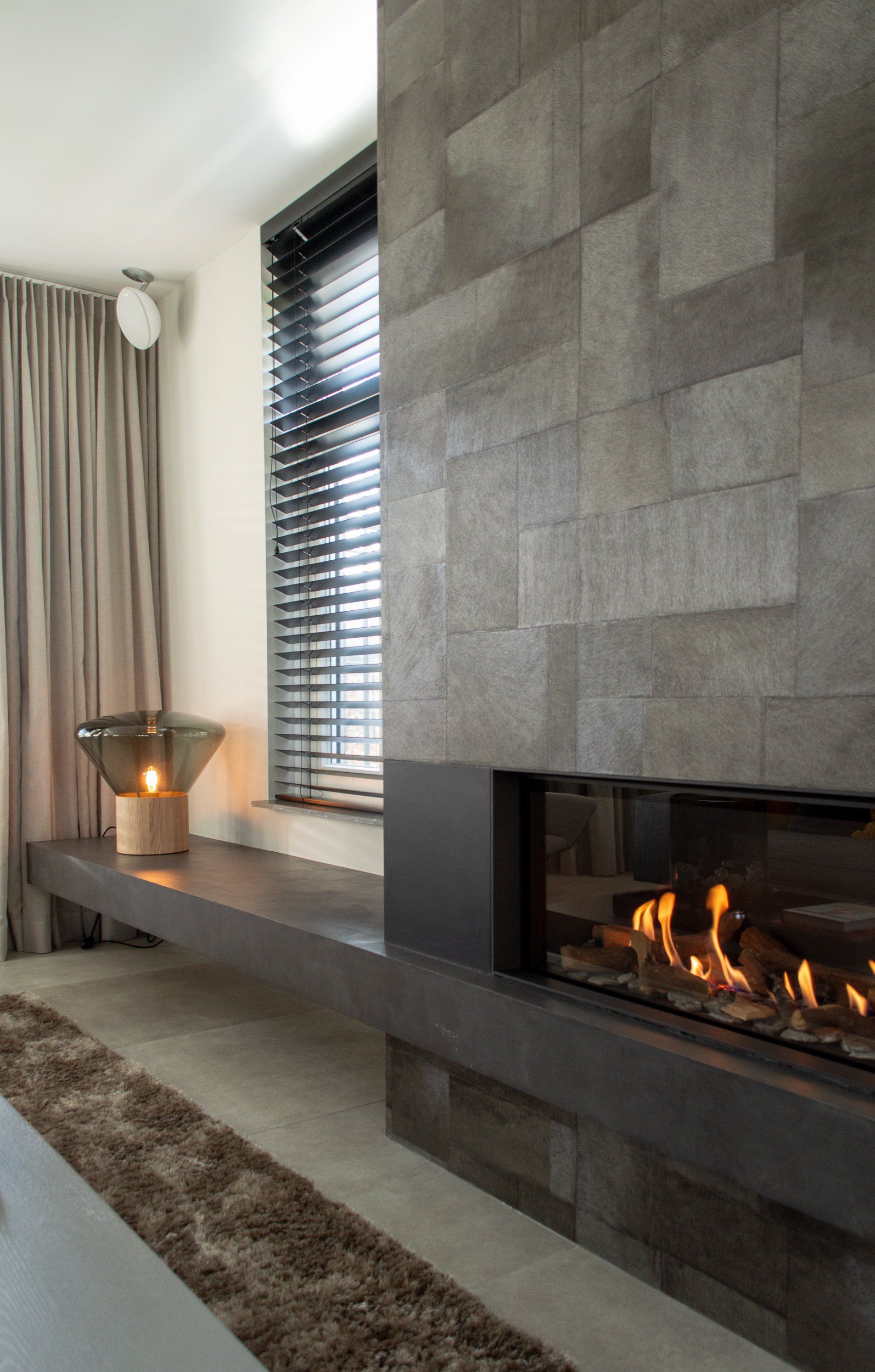 Een woonkamer met een open haard en een raam met jaloezieën.