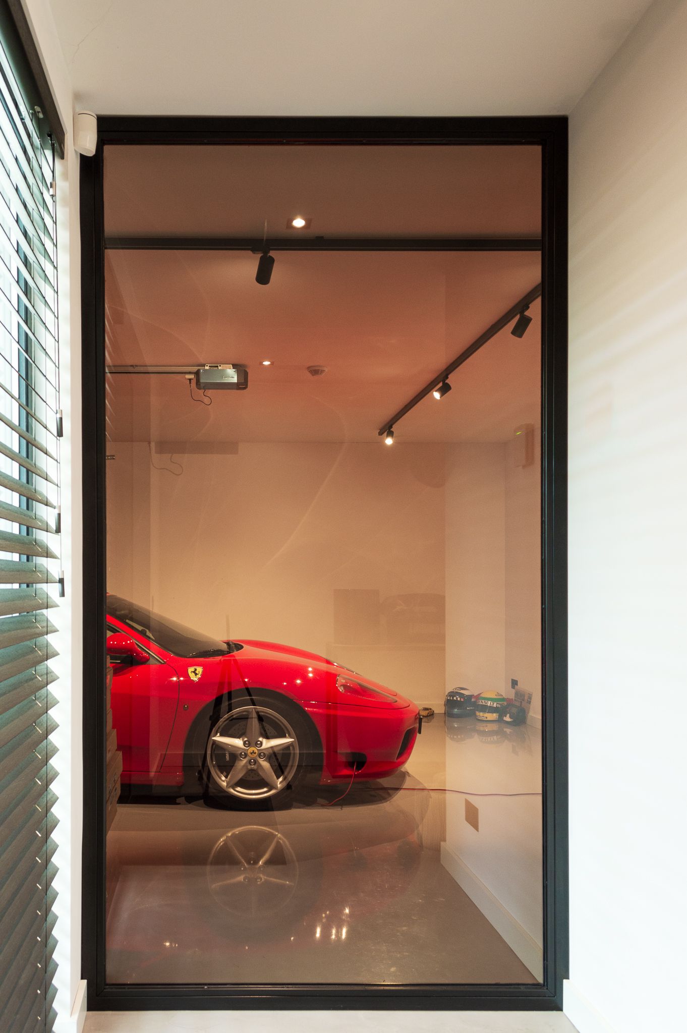 Een rode sportwagen staat geparkeerd in een garage achter een glazen raam.