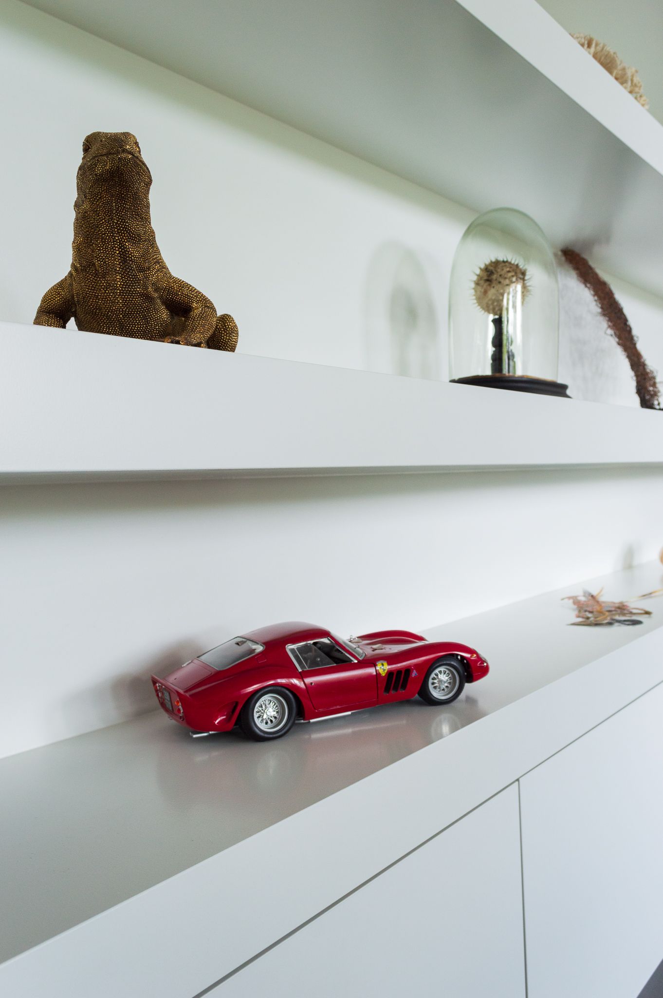 Een rode speelgoedauto staat op een witte plank.