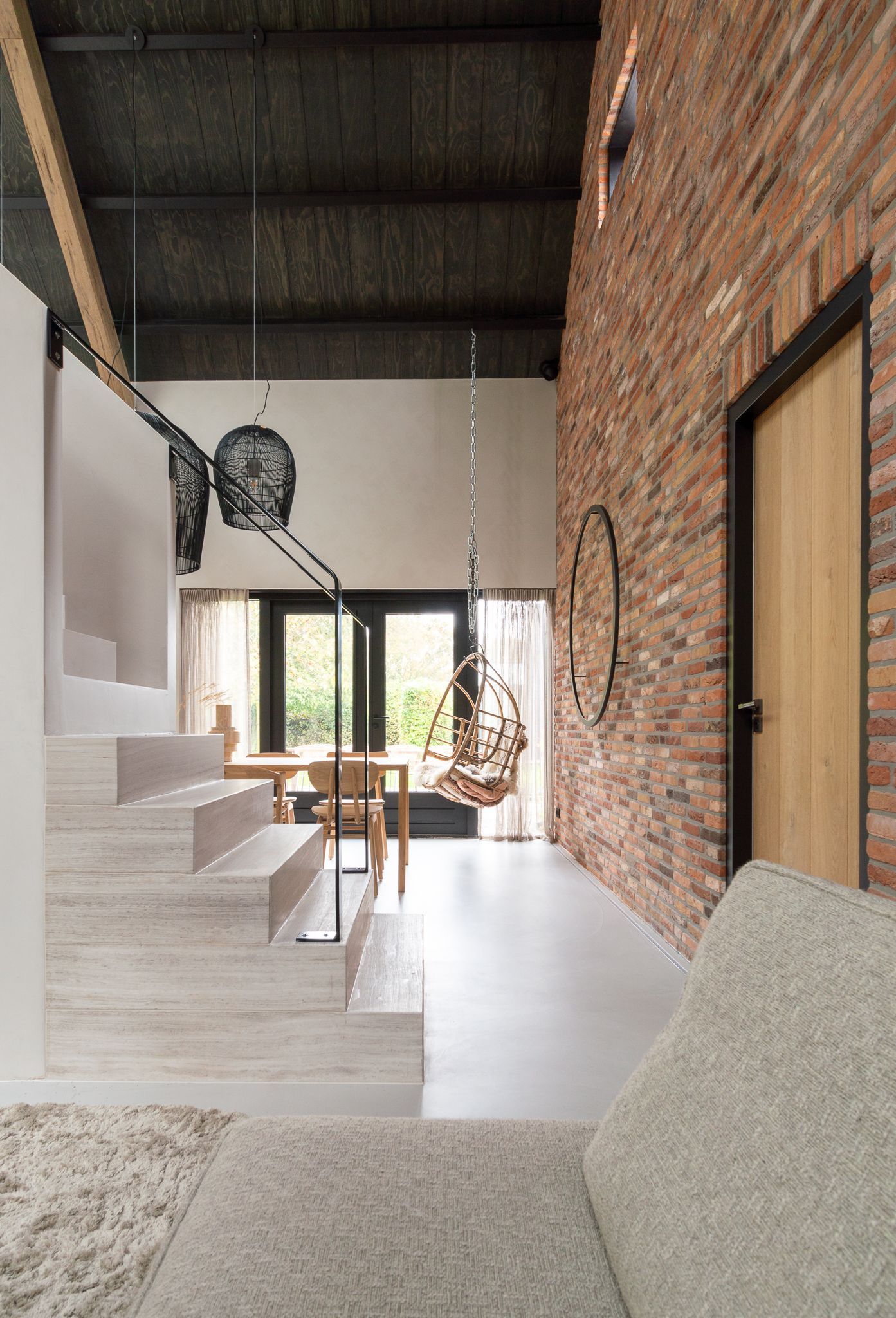 Een woonkamer met een trap naar de tweede verdieping en een bakstenen muur. Uit The Art of Living.