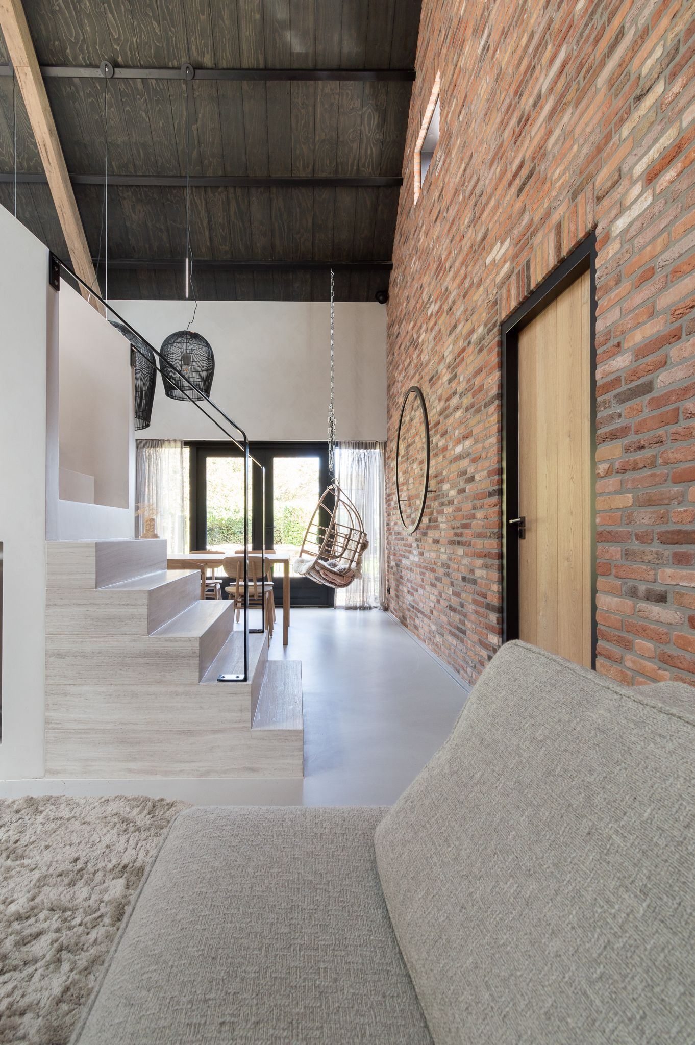 Een woonkamer met een bank, een marmeren trap en een bakstenen muur met verlichting van Jacco Maris en Ay Illuminate.