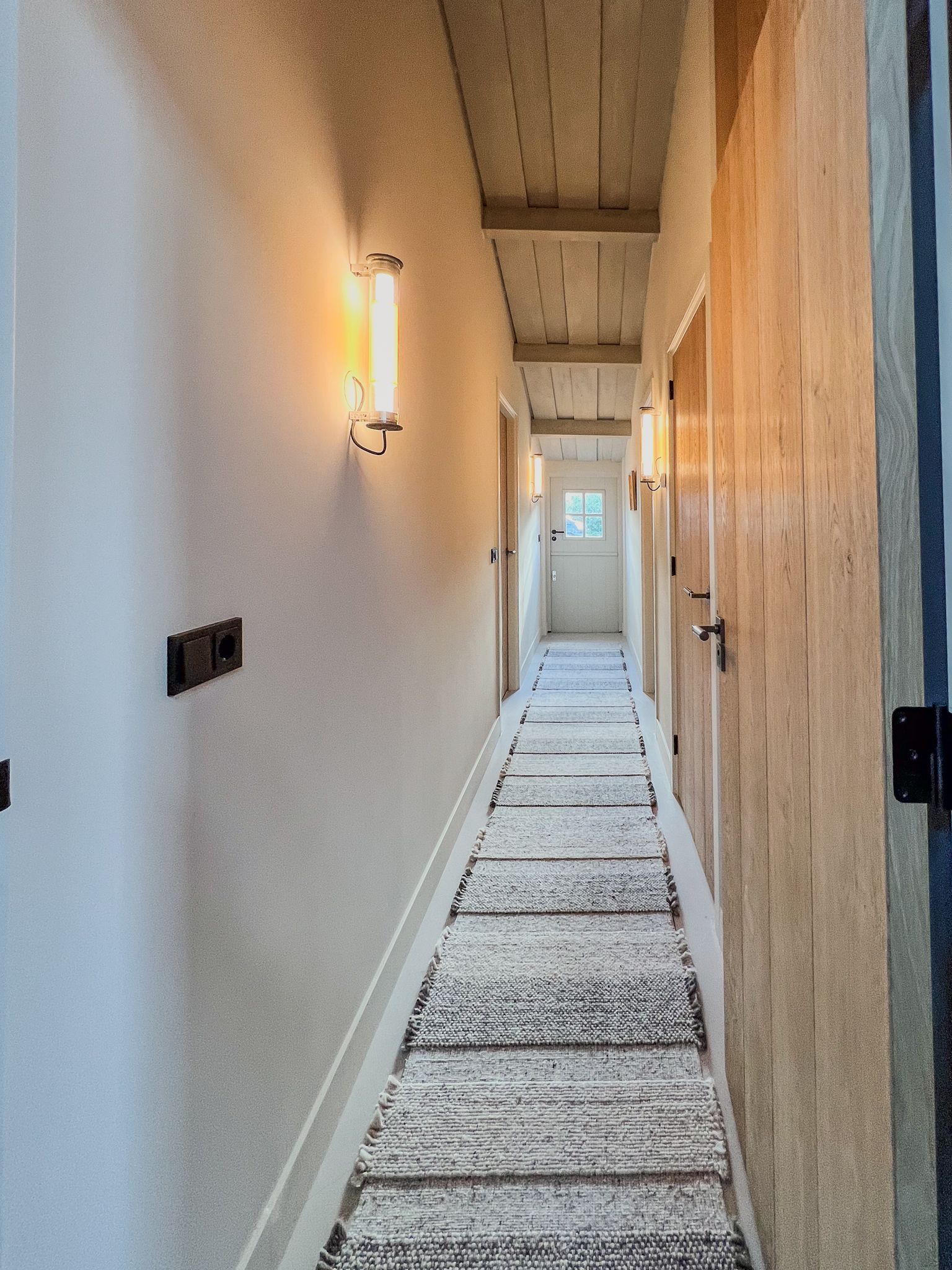 Een lange gang met een kleed op de vloer van Nova en een lamp aan de muur van DCW editions.