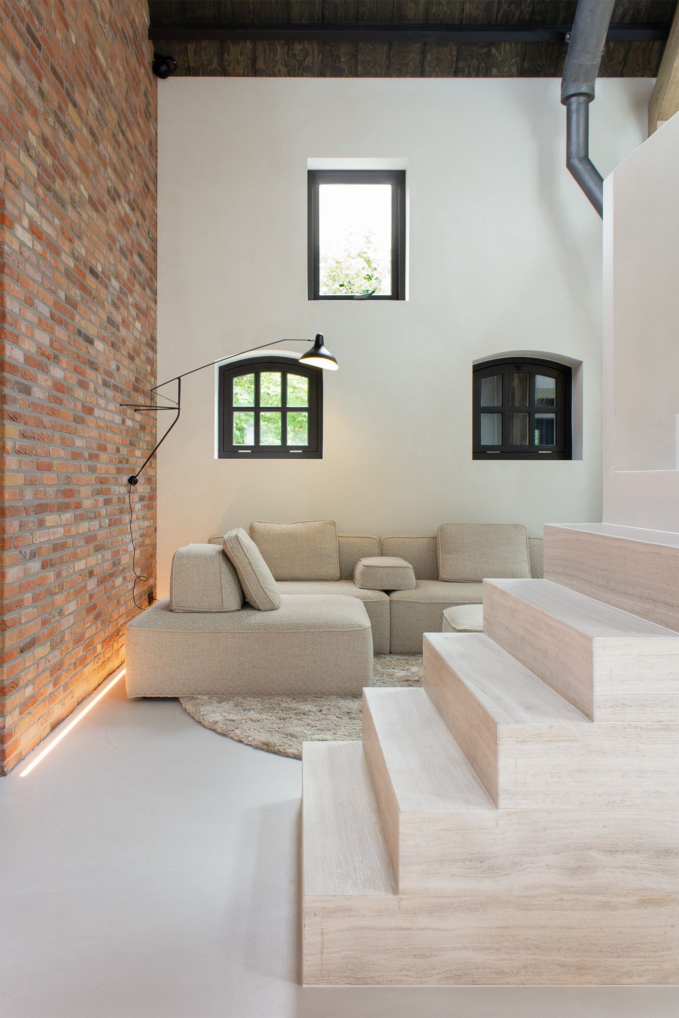 Een woonkamer met een bank van Vibieffe, een trap en een bakstenen muur met indirect licht ledlijn.