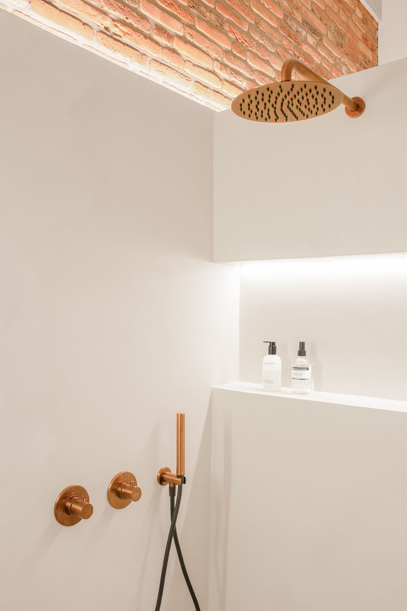 Een badkamer met douchekop en een bakstenen plafond.