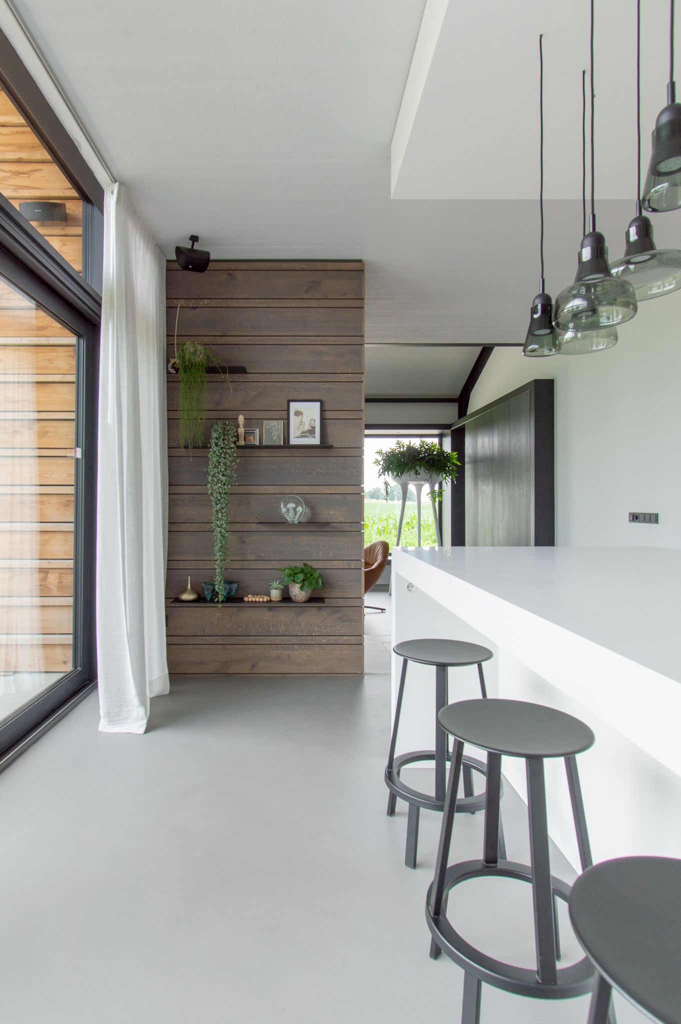 Een keuken met een lang aanrecht, krukken en een houten wand.