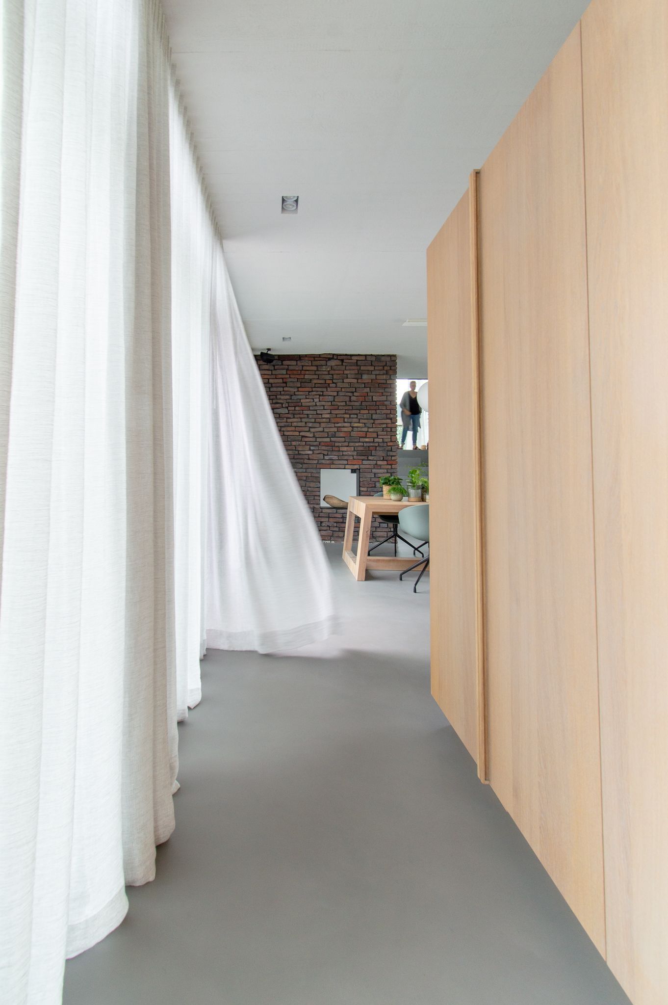 Een lange gang met mooie natuurlijke gordijnen en houten wanden die naar de woonkamer leidt.