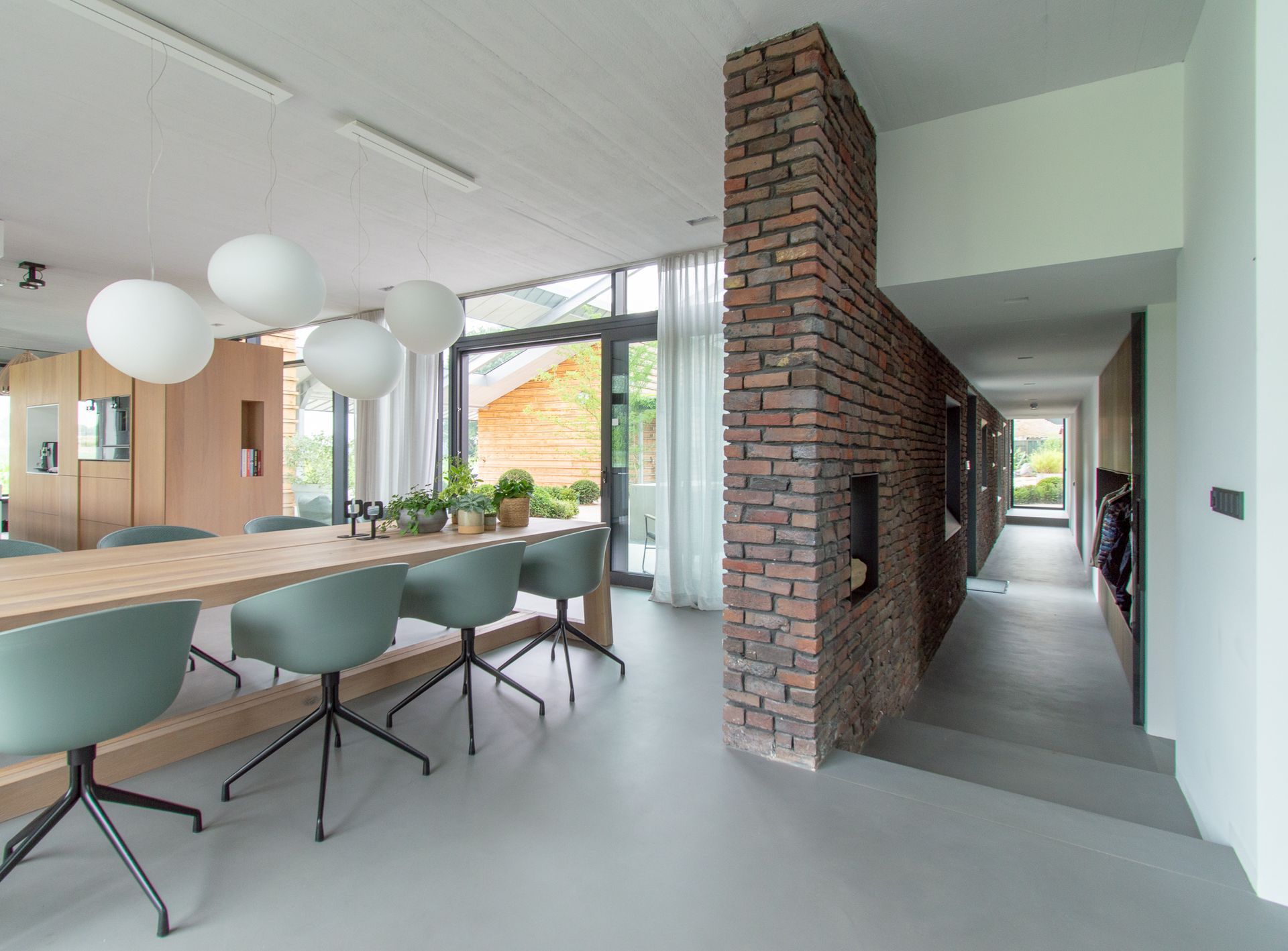 Een eetkamer met een lange tafel, stoelen en een bakstenen muur.
