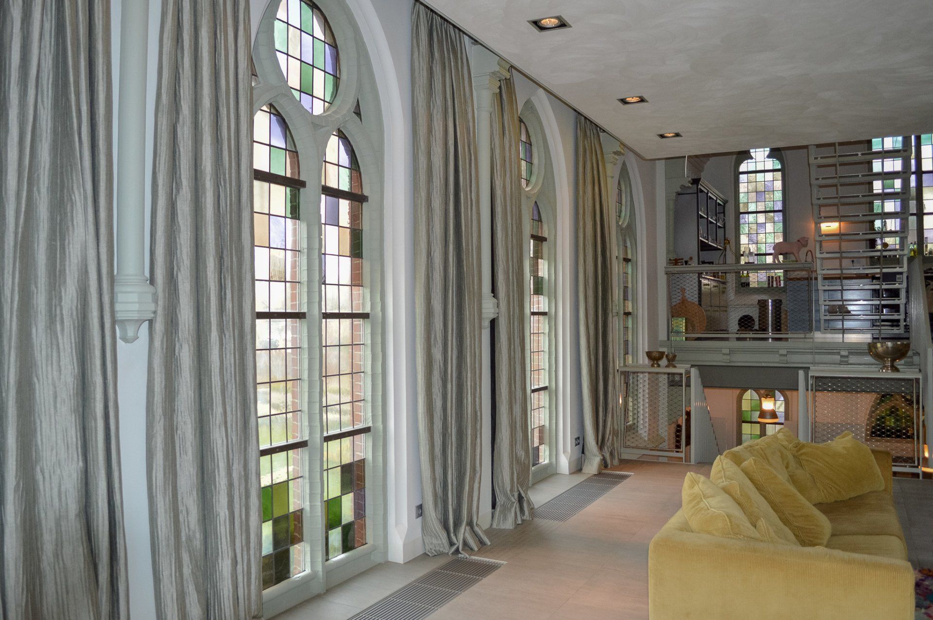 Een woonkamer met een gele bank en glas-in-loodramen