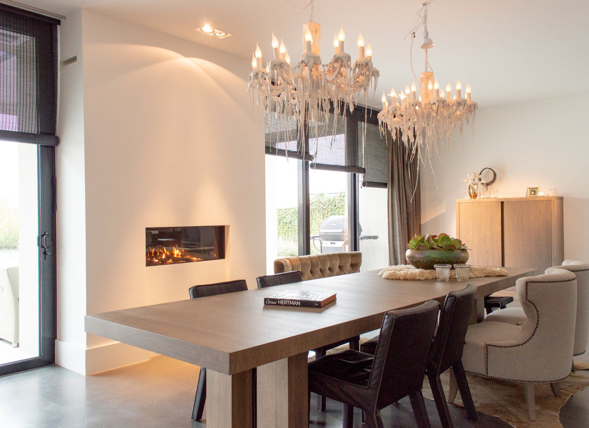 Een eetkamer met een lange tafel en stoelen en een kroonluchter die aan het plafond hangt