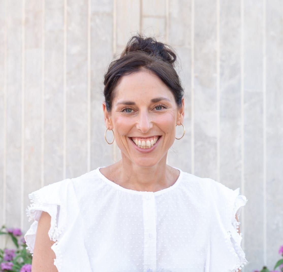 A woman in a white shirt and earrings is smiling for the camera.