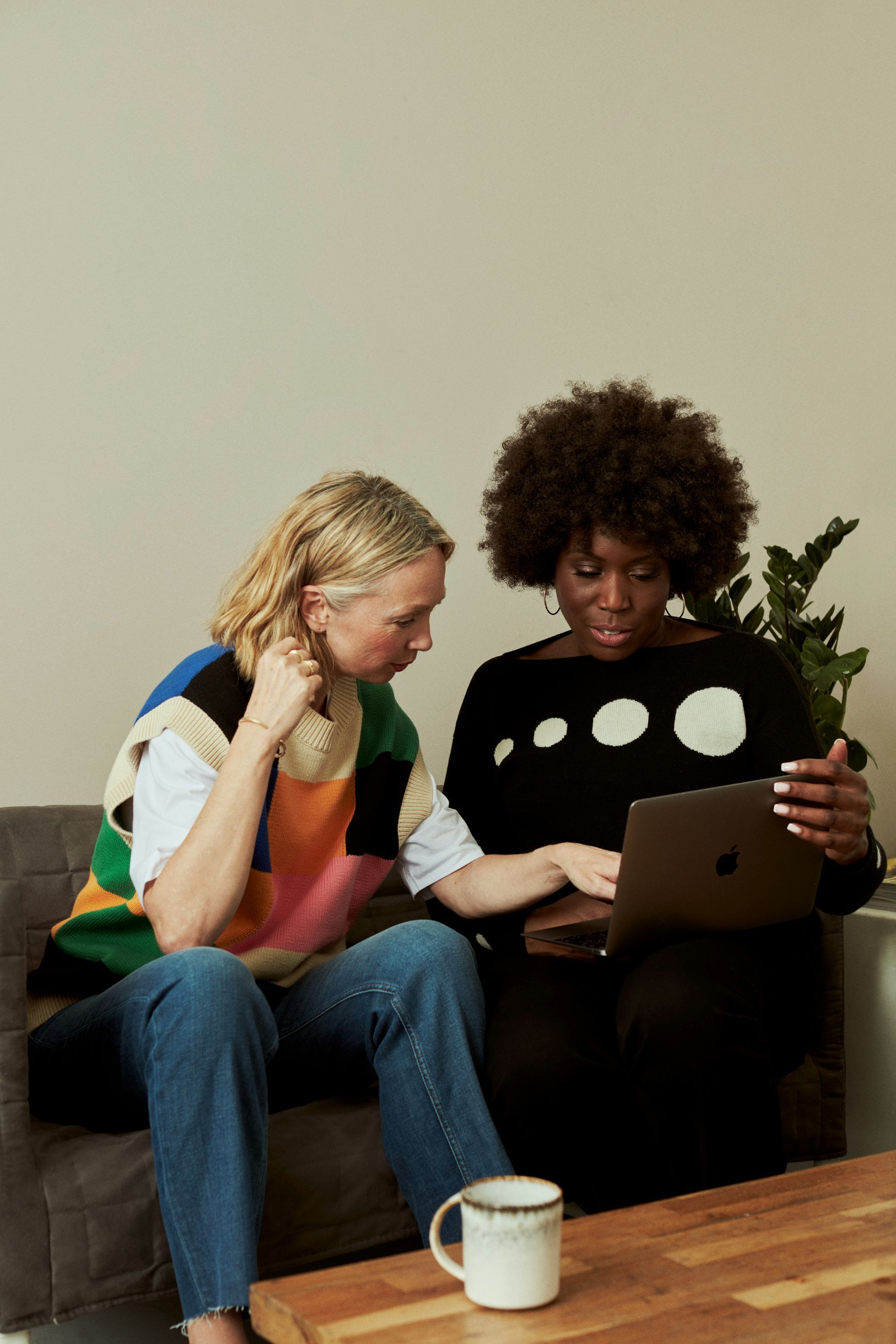 Two people on a couch looking at a laptop, with a mug on the floor nearby.