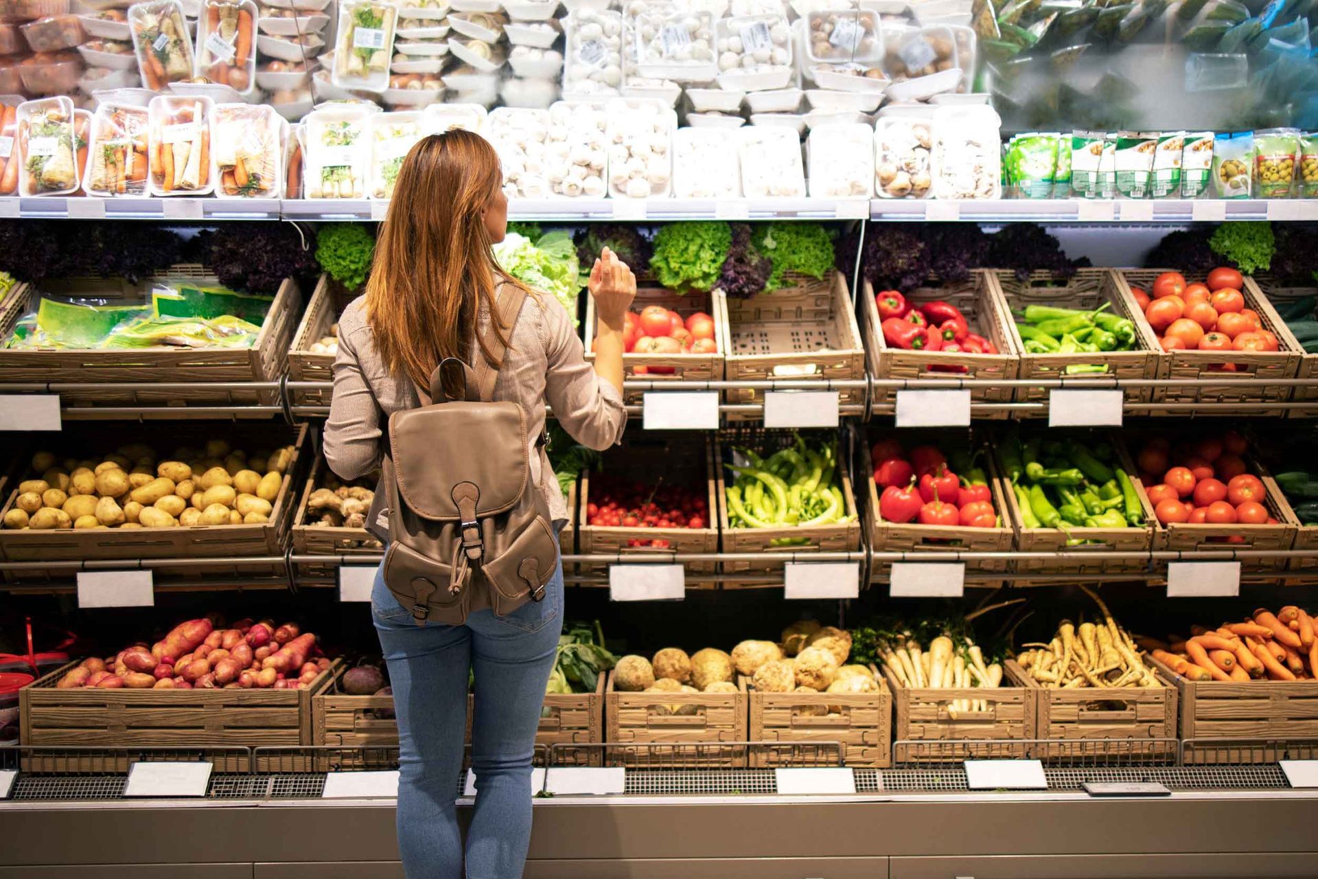 Customer selecting organic fruits and vegetables at a health food store with fresh produce bins.