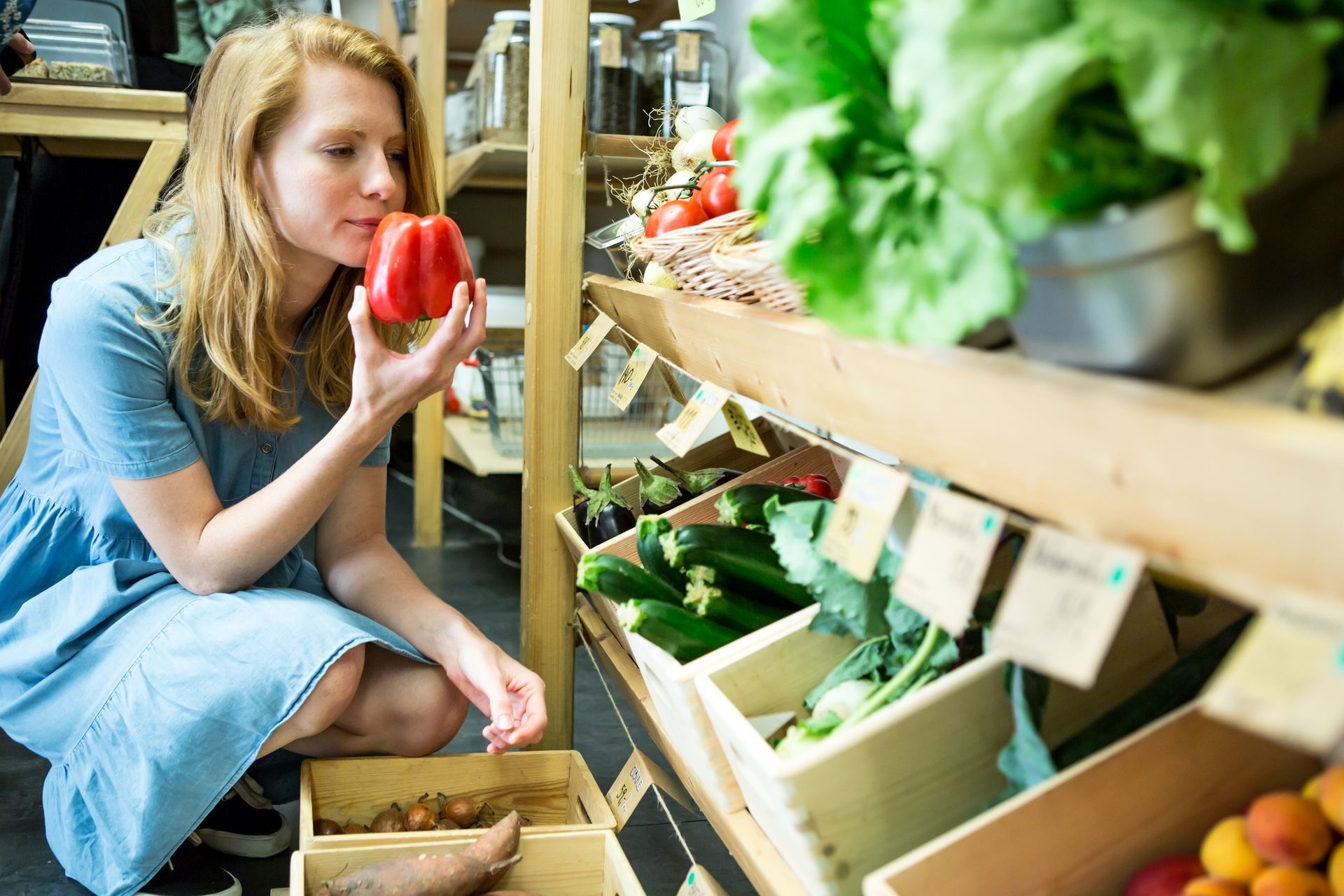 Person in blue dress holding red pepper in grocery store.