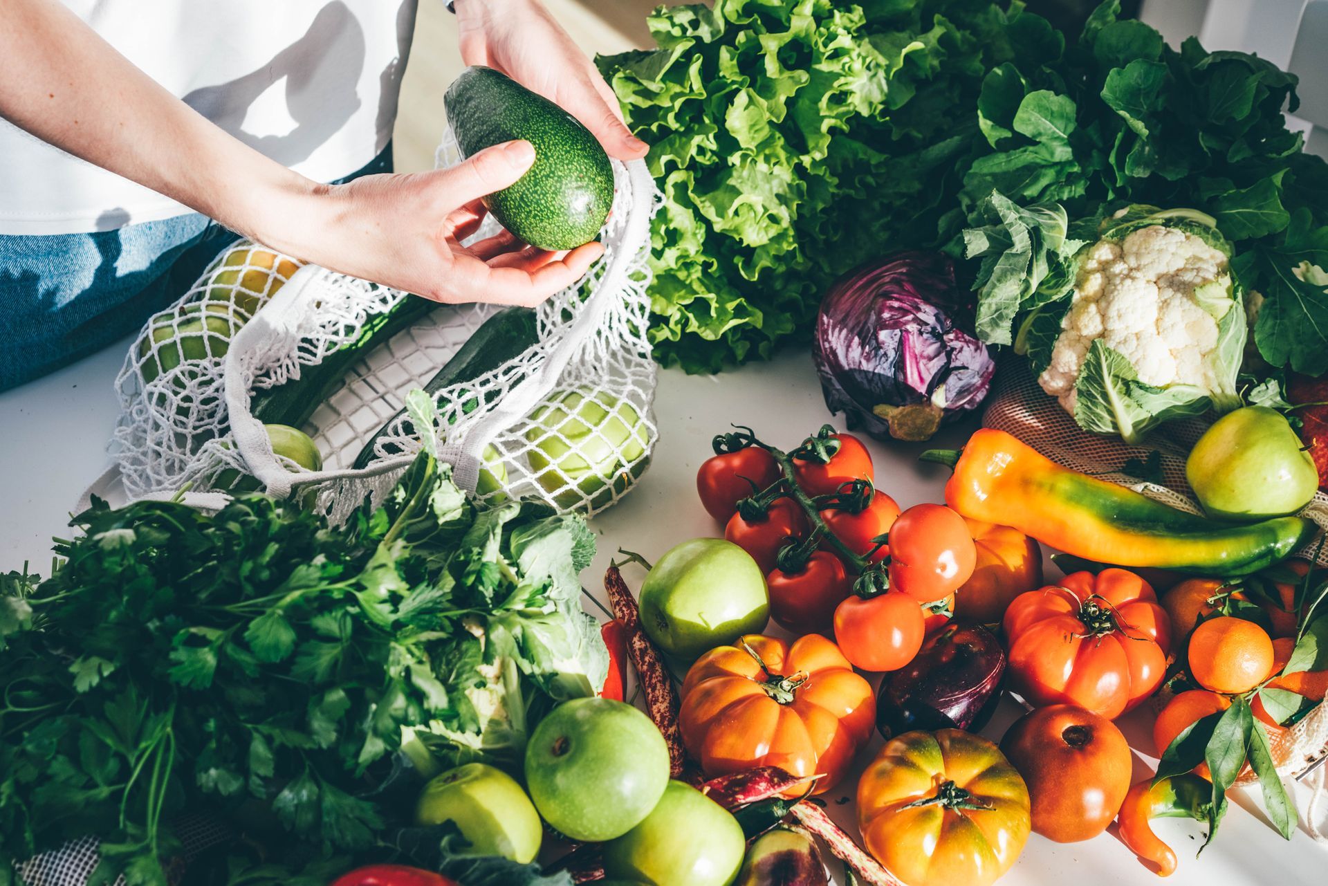 Woman taking fresh organic vegetables out of a mesh bag, putting them on the kitchen table at home.