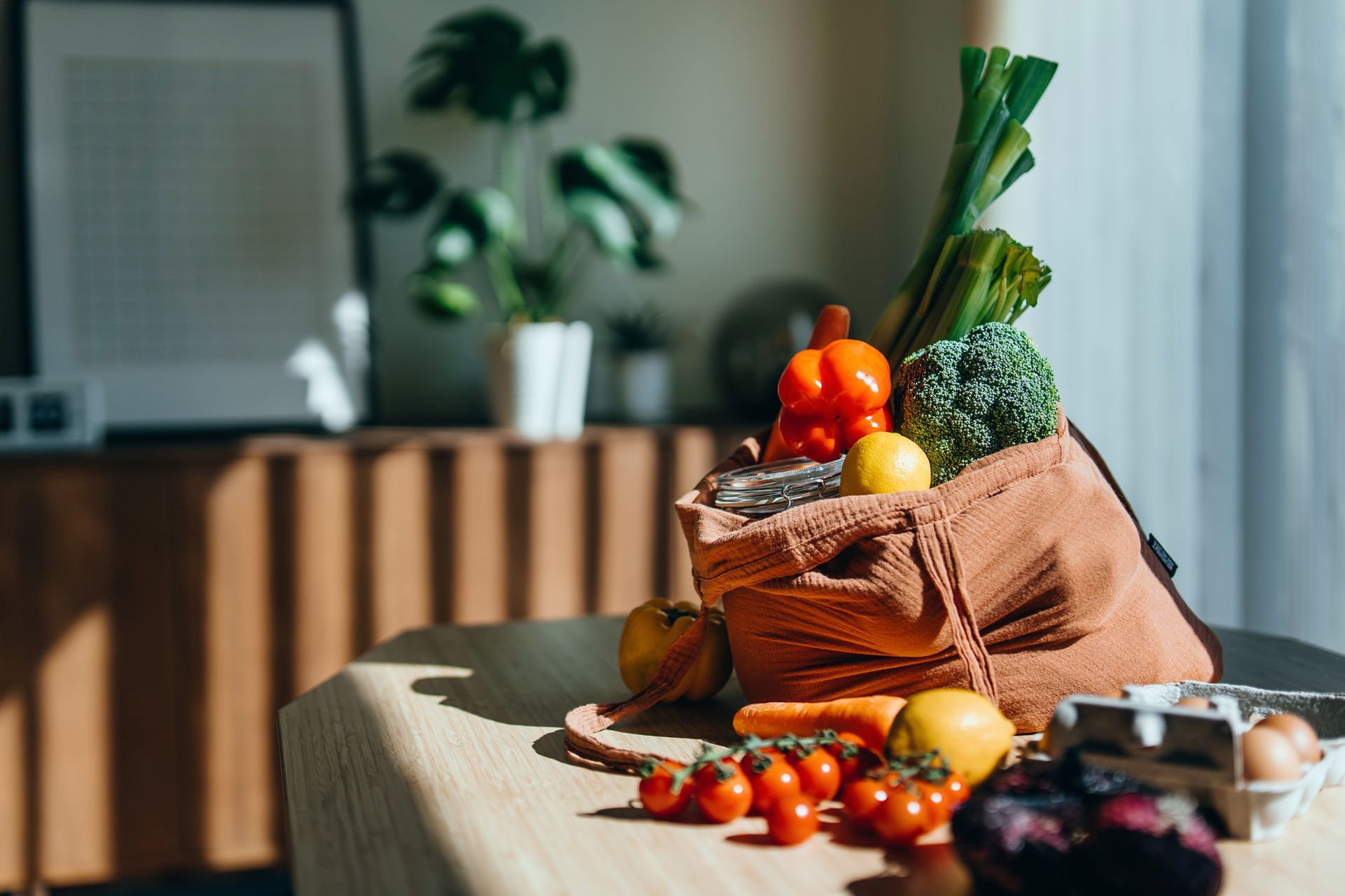 A shopping bag with multi-colored fresh vegetables and groceries on a table.