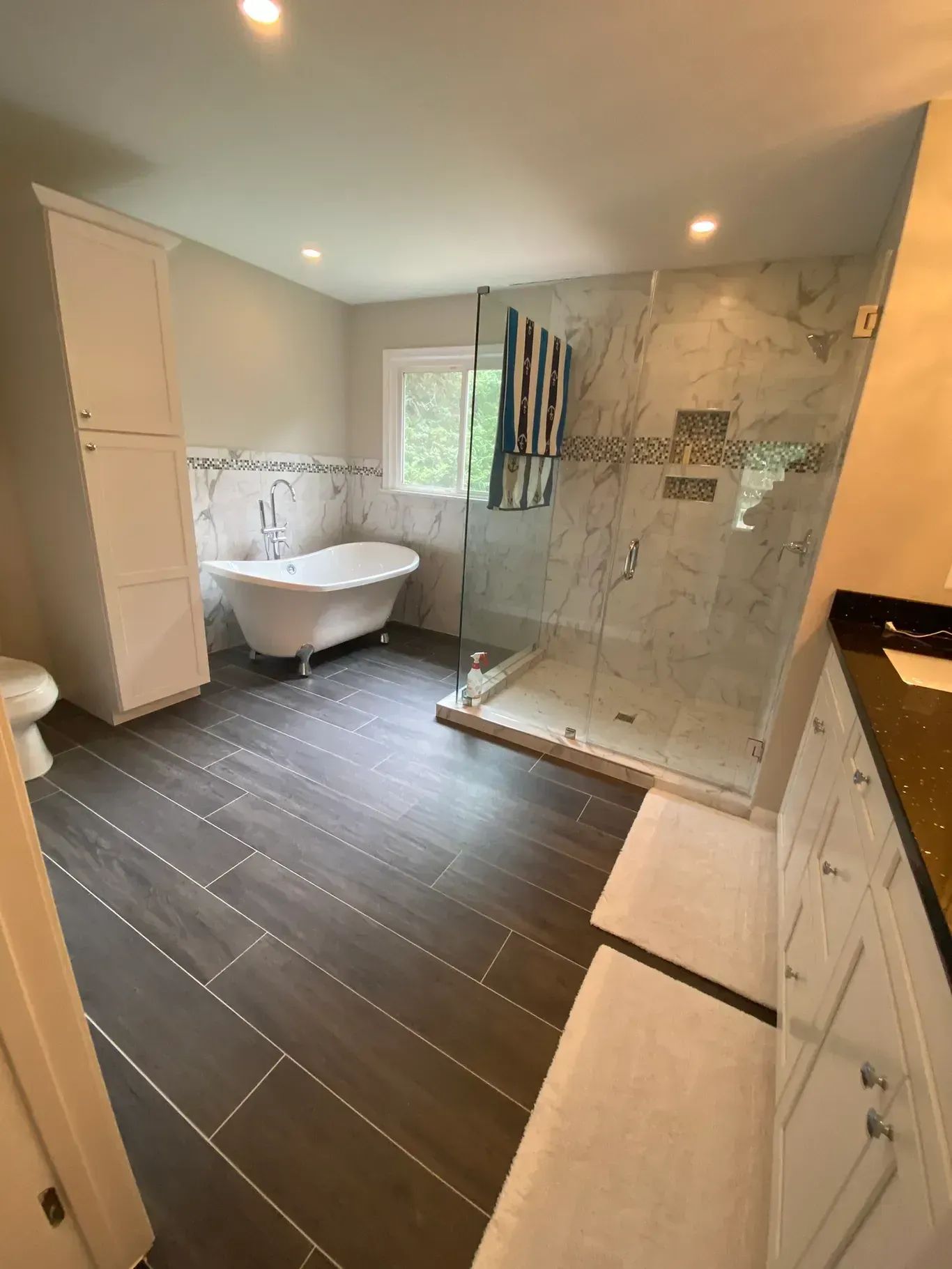 Bathroom with dark tile floor, white cabinets, clawfoot tub, glass shower, and marble walls.