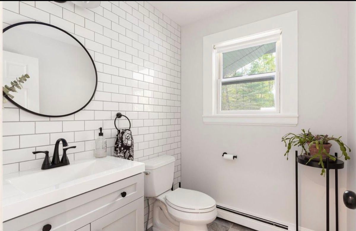 A bathroom with a toilet , sink , mirror and window.