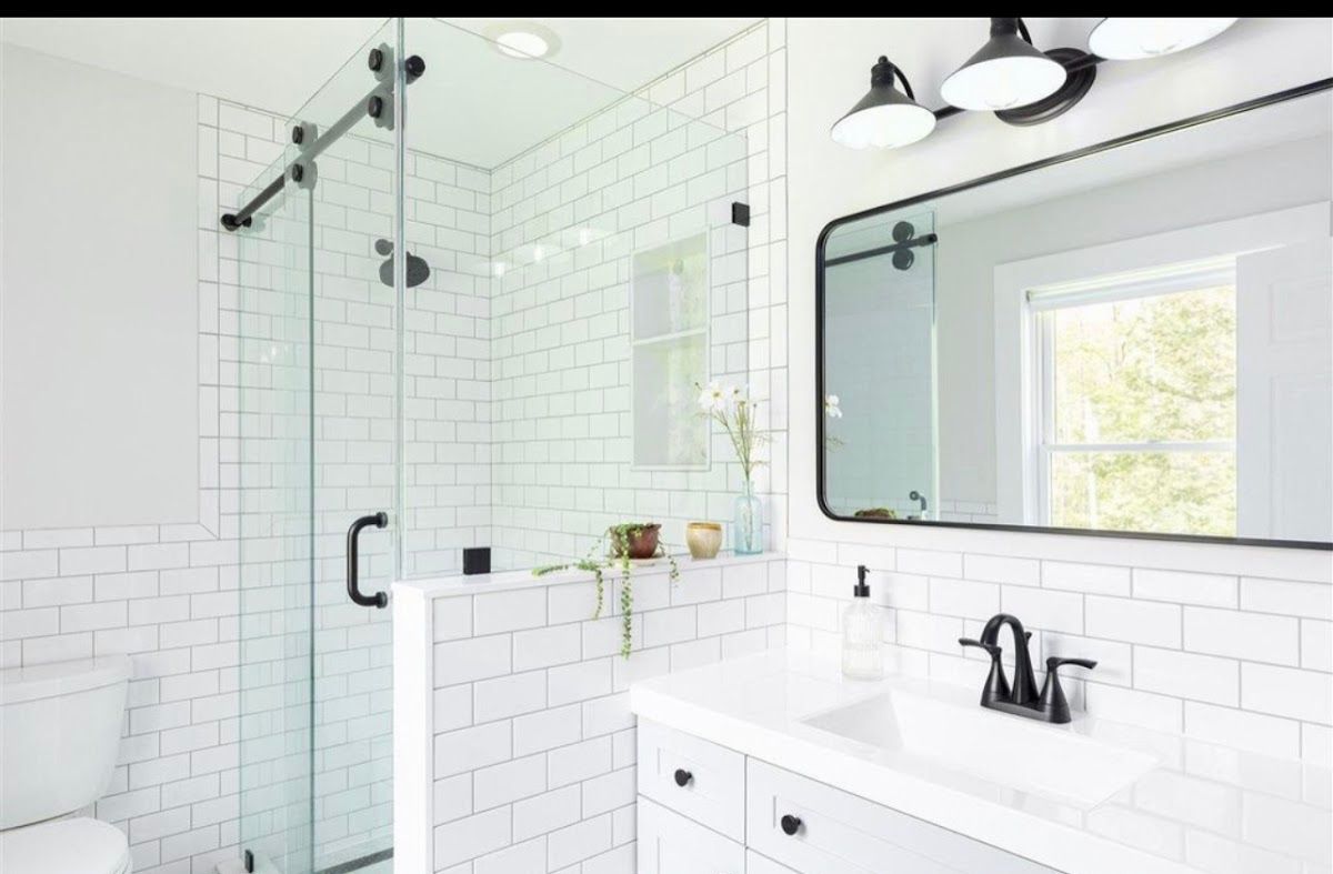 A bathroom with white tiles , a sink , a toilet and a mirror.