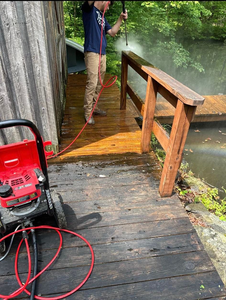 A man is cleaning a wooden bridge with a high pressure washer.