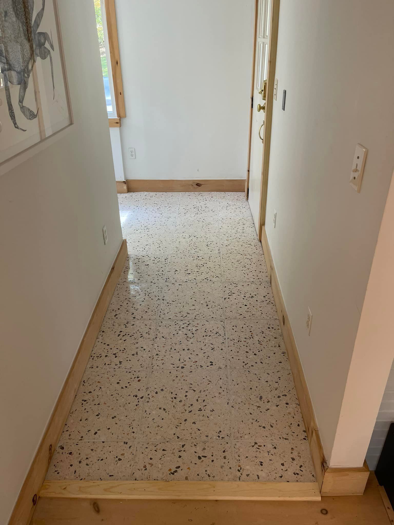 A hallway with a white tile floor and wooden trim.