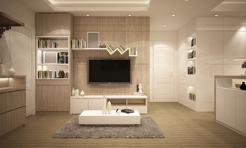 Modern living room with light wood and white furniture. TV on wall, bookshelves, rug.