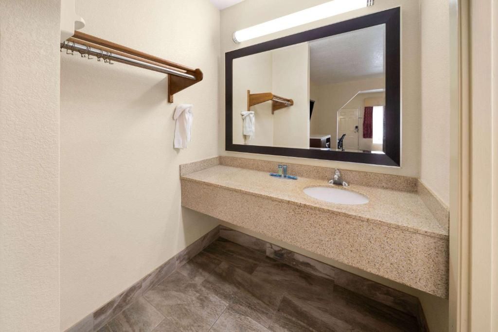 Bathroom with a beige countertop, large mirror, and a towel rack. Gray-brown tiled floor.