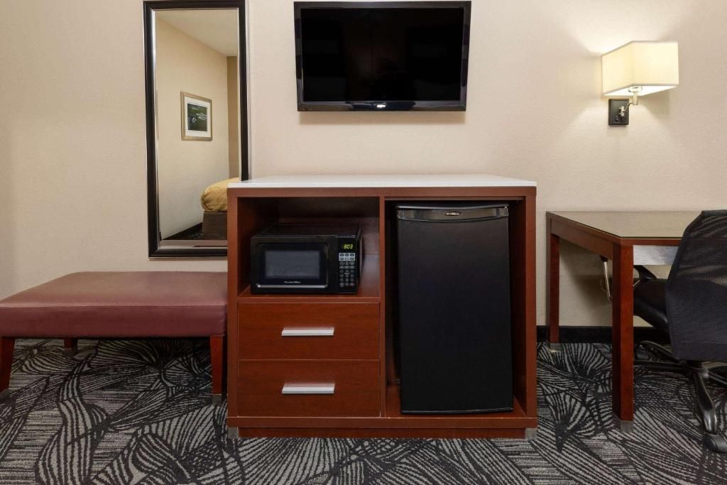 Hotel room: microwave and mini-fridge in a wooden cabinet, TV, desk, mirror, and a bench.