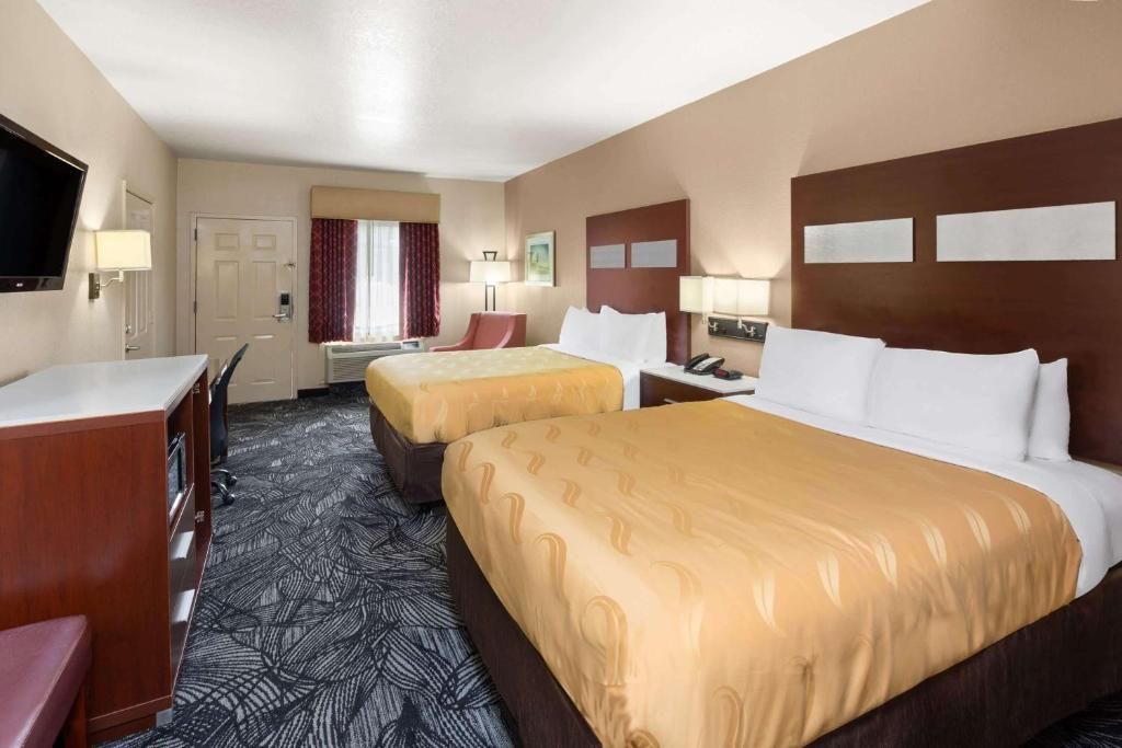Hotel room with two queen beds, desk, TV, and neutral color scheme.