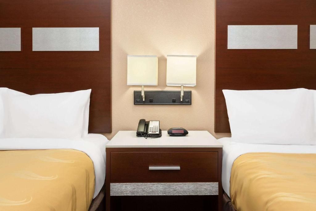 Two beds with yellow covers in a hotel room, a nightstand with a phone, and wall sconces.