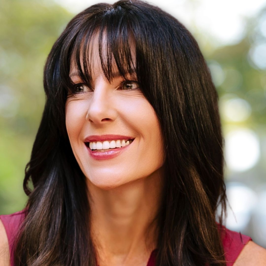 SmileArt patient with dark hair smiles, looking off-camera. She wears a maroon top and is outdoors with a blurred background.