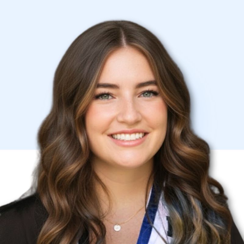 Woman with long, wavy brown hair smiles at the camera, wearing a black top and a necklace.