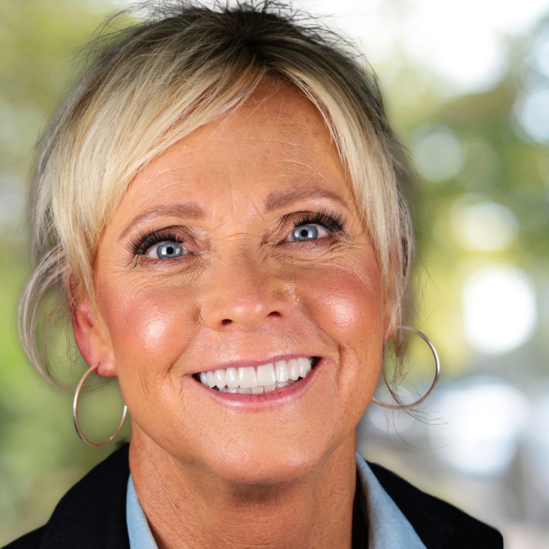 SmileArt patient with blonde hair and large hoop earrings smiles at the camera, blurred background.